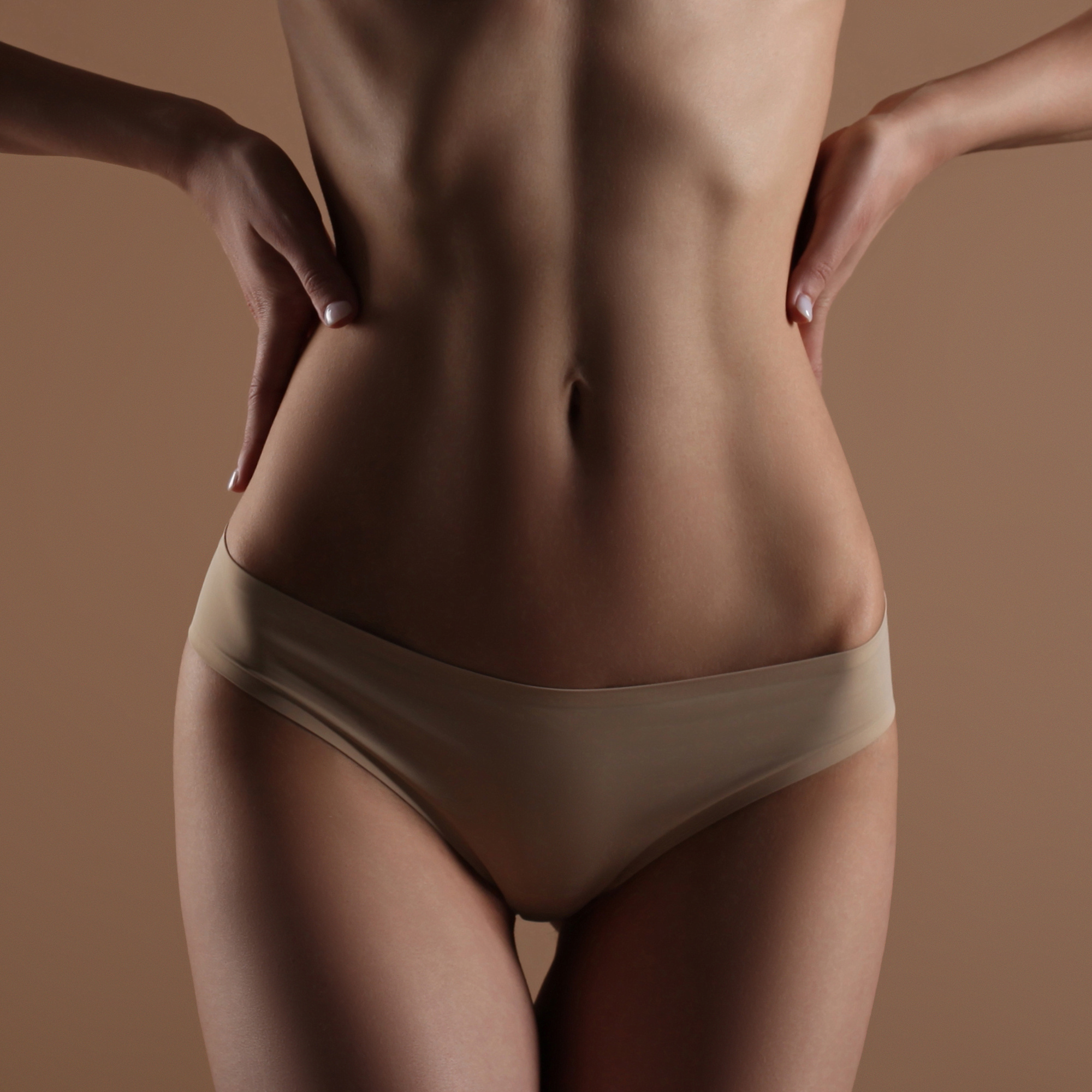 Skinny young woman in lingerie holds her hands on her waist. Front view on beige background. Fitness, diet, skin and body care | Ella Esthetics in Alexandria, VA
