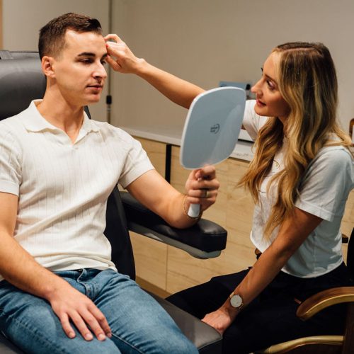 Man with Mirror in hand and Breanna Injector touching his forehead in a clinic | Ella Esthetics in Alexandria, VA